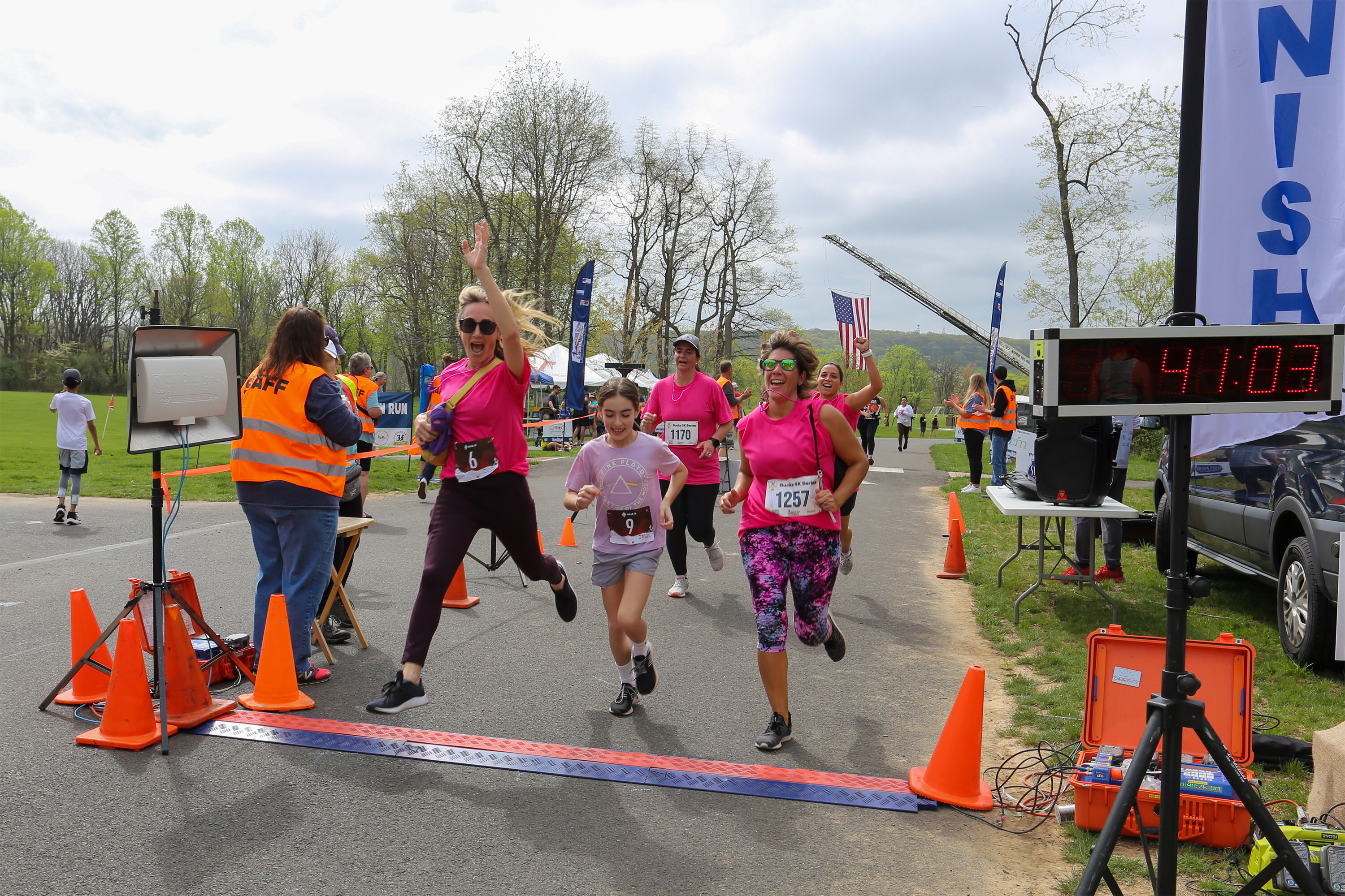 Runners in pink shirts leaping with joy as they cross the finish line at the Be Kind 5K